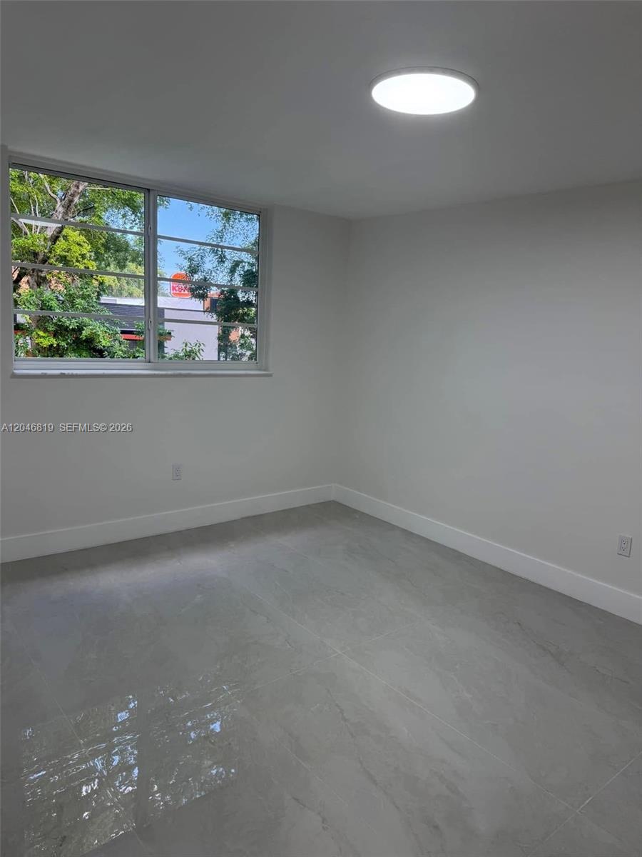 A minimalist bedroom features light gray tile flooring, white walls, and a large window — 14155 SW 87th St # E202, Miami FL 33183, MIAMI, FL