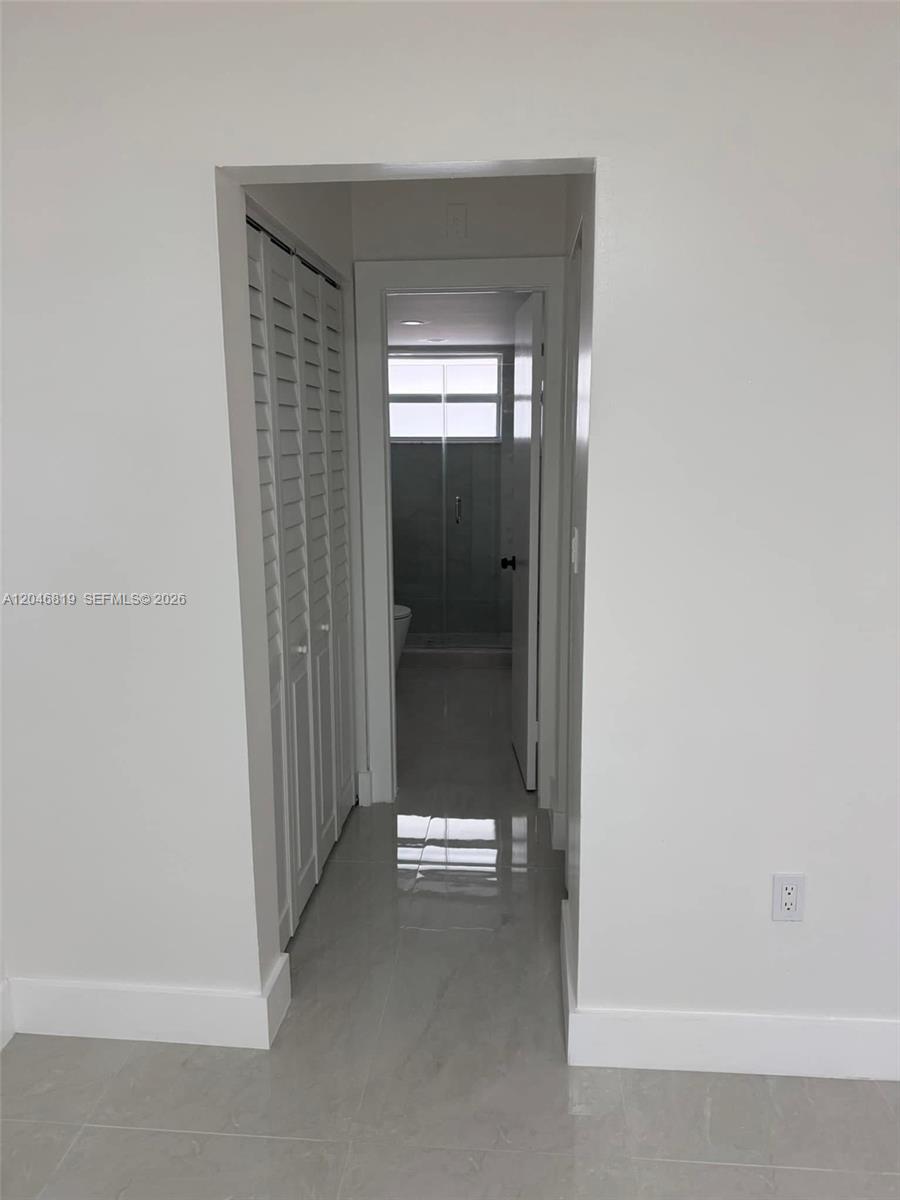 A hallway with white walls and light tile flooring leads to a bathroom — 14155 SW 87th St # E202, Miami FL 33183, MIAMI, FL