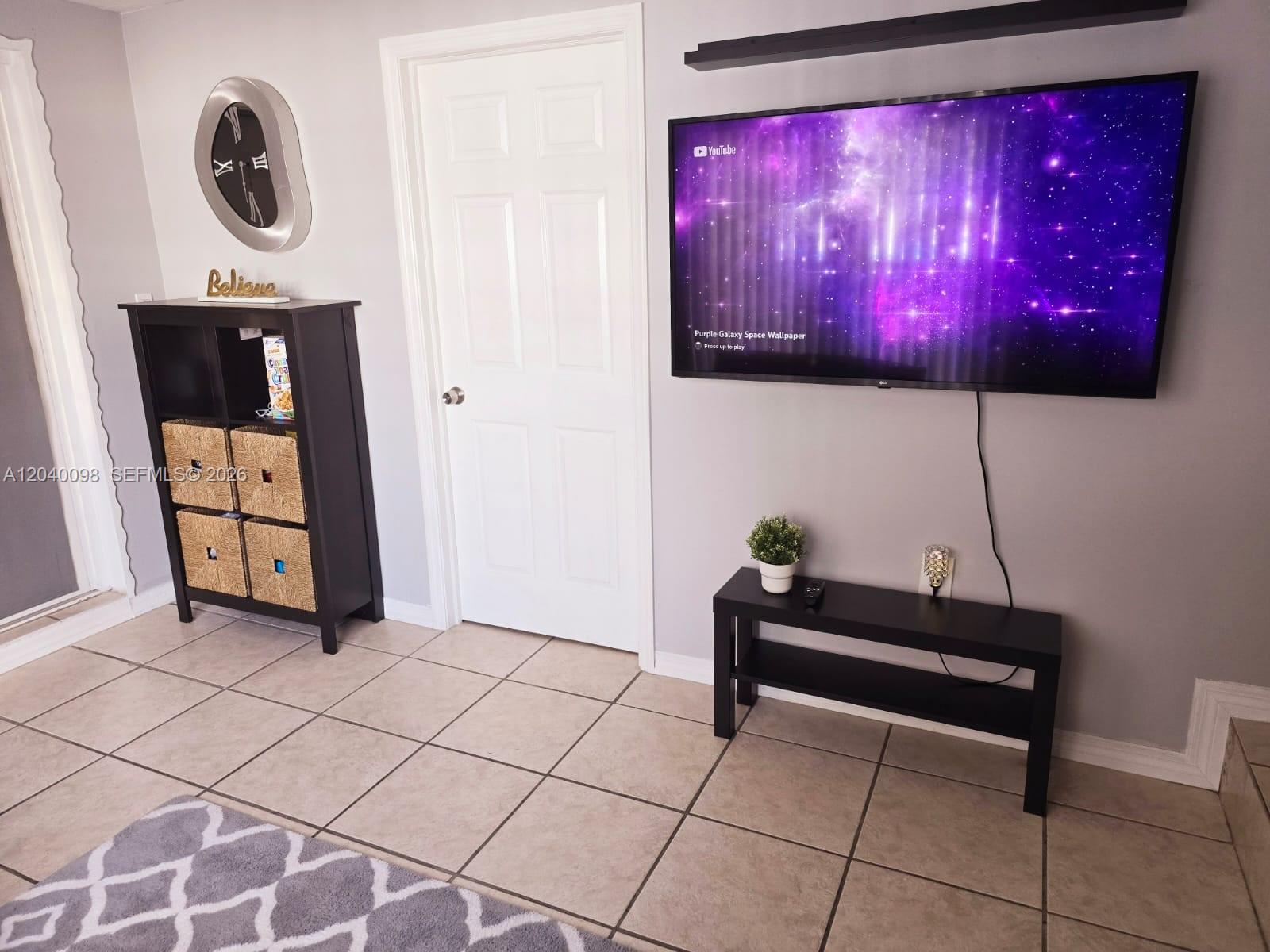 A living room features a wall-mounted television, a storage shelf with baskets, and tiled flooring — 4074 NW 4th St, Miami FL 33126, MIAMI, FL