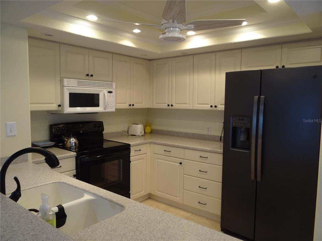 A kitchen features white cabinets, granite countertops, and black appliances under a ceiling fan — 601 SHREVE STREET UNIT 41C, PUNTA GORDA, FL