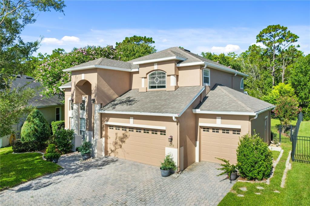 A two-story tan stucco house features a three-car garage and a paved driveway — 1473 AMARYLLIS CIRCLE, ORLANDO, FL