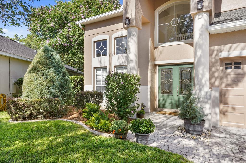 A tan two-story house features a paver walkway, green double front doors, and landscaping — 1473 AMARYLLIS CIRCLE, ORLANDO, FL