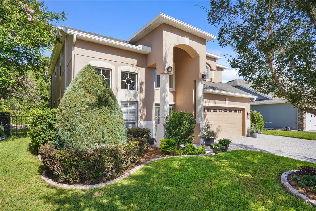 A two-story tan stucco house with a two-car garage and a landscaped front yard — 1473 AMARYLLIS CIRCLE, ORLANDO, FL