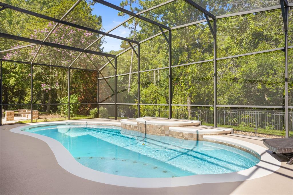 A screened-in swimming pool with a raised spa and stone tile accents sits outdoors — 1473 AMARYLLIS CIRCLE, ORLANDO, FL