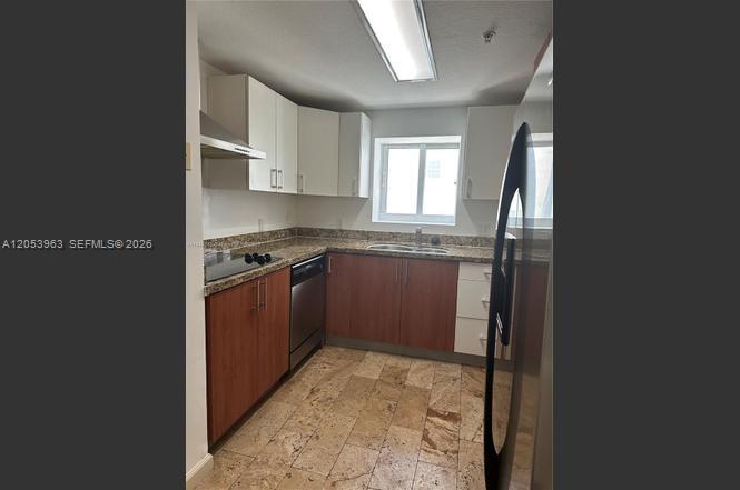 A kitchen features wood-toned lower cabinets, white upper cabinets, stainless steel appliances, and stone flooring — 170 SE 14th St # 2604, Miami FL 33131, MIAMI, FL