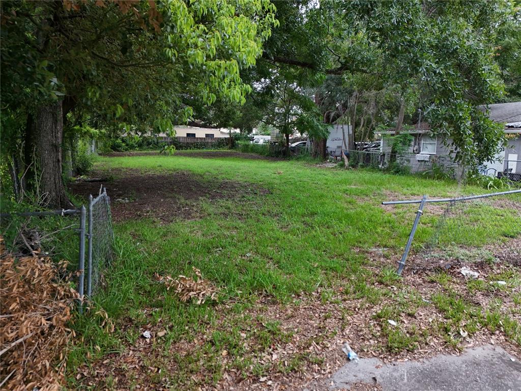 A grassy, fenced-in vacant lot is surrounded by trees and neighboring residential buildings — 1413 29TH STREET, ORLANDO, FL