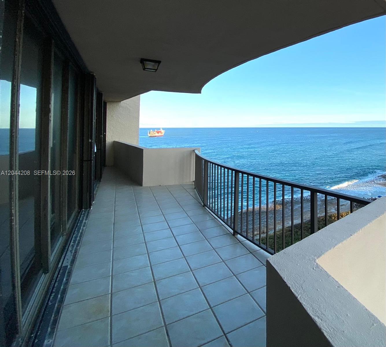 A tiled balcony overlooks the ocean with a metal railing and a ship in view — 4200 N Ocean Dr # 1103, Riviera Beach FL 33404, RIVIERA BEACH, FL