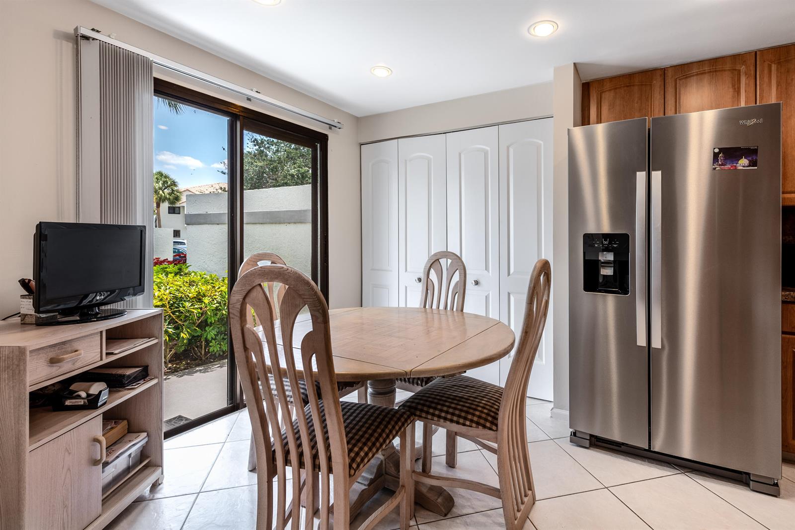A dining area features a round wooden table, four chairs, a refrigerator, and sliding glass doors — 15831 Loch Maree Lane # 5502, Delray Beach FL 33446, DELRAY BEACH, FL