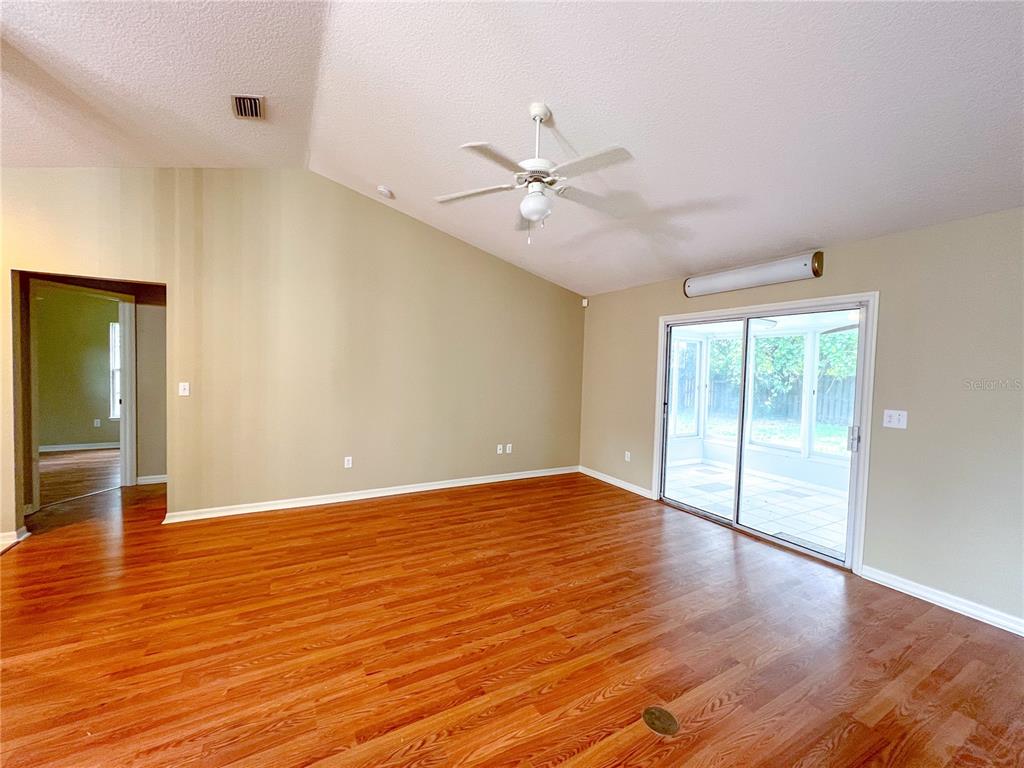 An empty living room features vaulted ceilings, a ceiling fan, wood flooring, and sliding glass doors — 8414 SW 66TH LANE, GAINESVILLE, FL