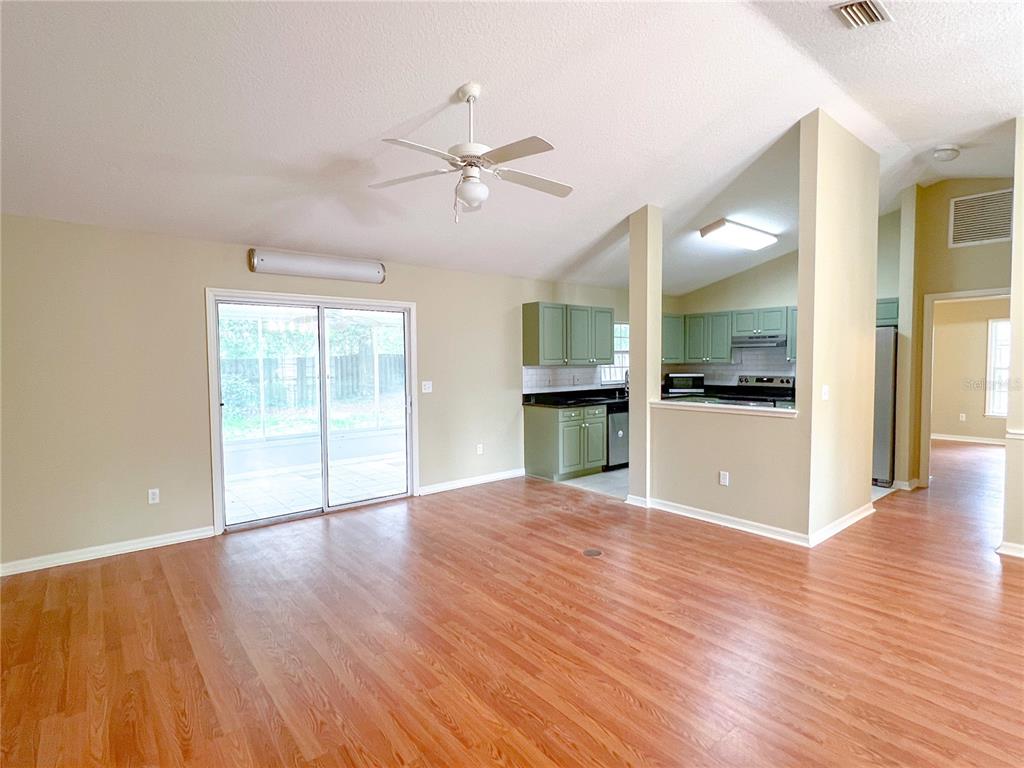 A living room with wood-look flooring, a ceiling fan, and an adjacent kitchen with green cabinets — 8414 SW 66TH LANE, GAINESVILLE, FL