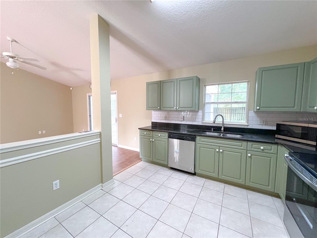 A kitchen features sage green cabinets, black countertops, stainless steel appliances, and white tile flooring — 8414 SW 66TH LANE, GAINESVILLE, FL