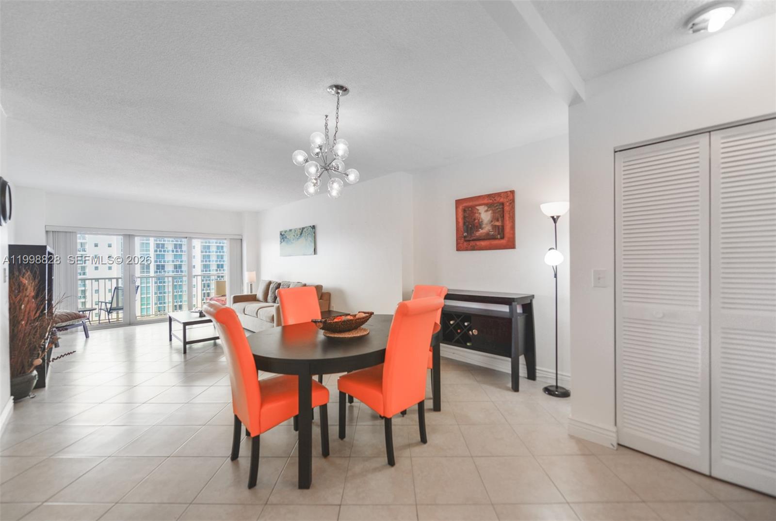 A dining area with orange chairs and a chandelier sits adjacent to a living room — 1965 S Ocean Dr # 14D, Hallandale Beach FL 33009, HALLANDALE BEACH, FL