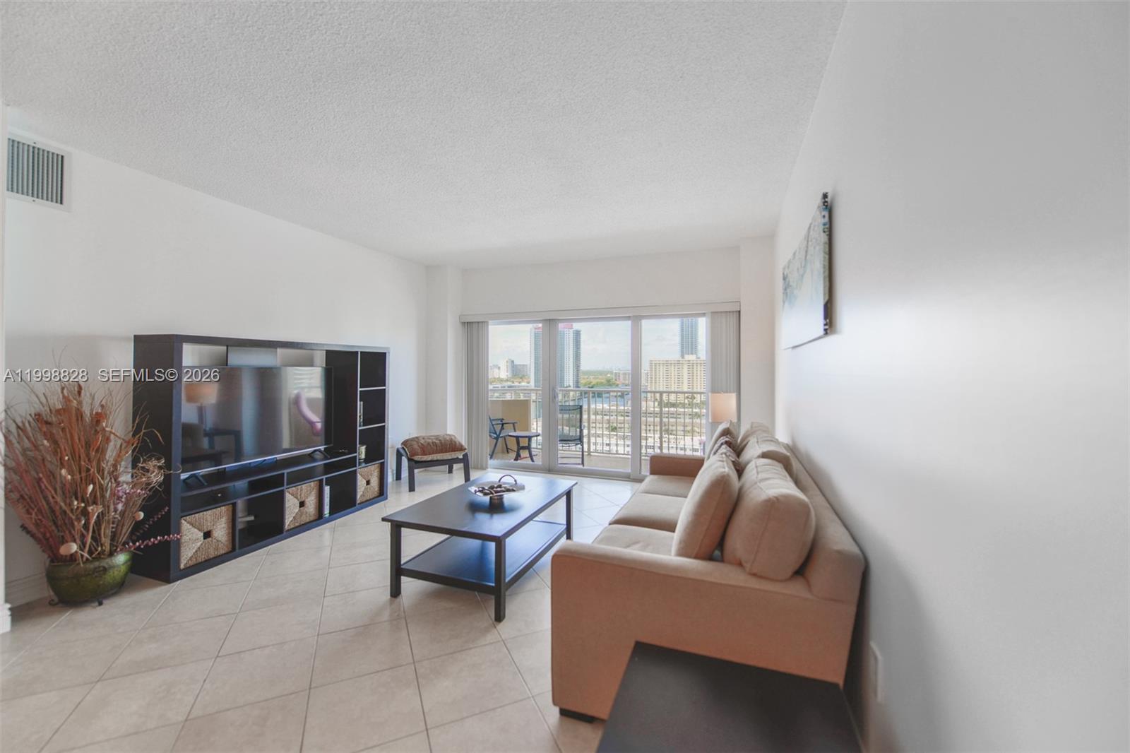 A living room features a beige sofa, dark media console, coffee table, and balcony access — 1965 S Ocean Dr # 14D, Hallandale Beach FL 33009, HALLANDALE BEACH, FL