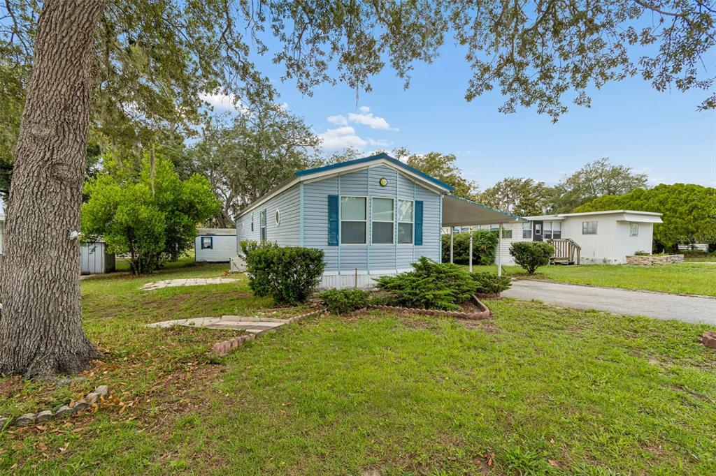 A light blue mobile home sits on a grassy lot with a carport and trees — 34992 FRASER STREET, DADE CITY, FL