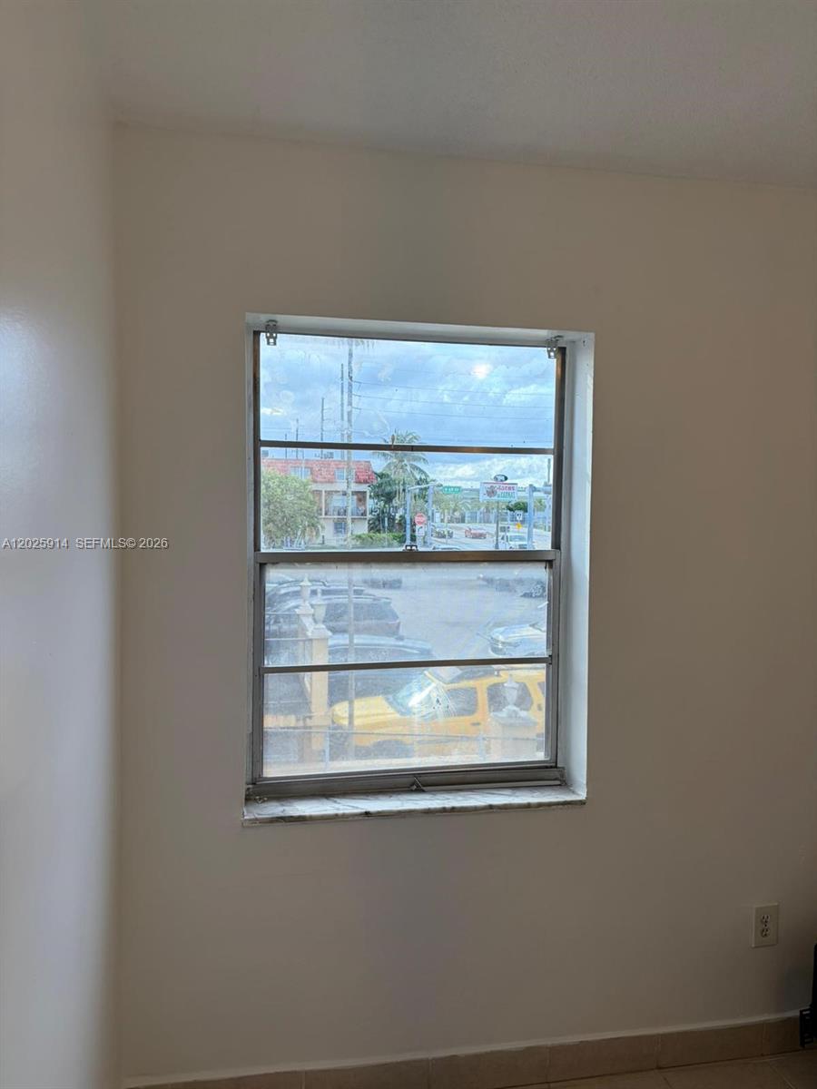 A window with horizontal slats overlooks a parking lot and street from a plain room — 6820 W Flagler St # 212, Miami FL 33144, MIAMI, FL