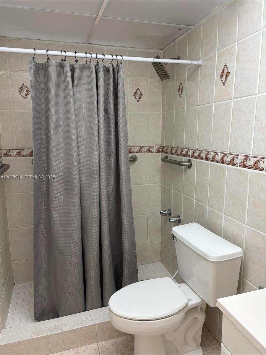 A bathroom features a tiled shower stall with a curtain, a toilet, and wall-mounted grab bars — 6820 W Flagler St # 212, Miami FL 33144, MIAMI, FL