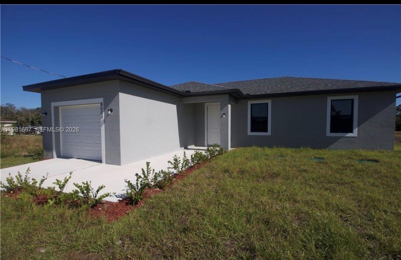 A single-story house with a gray stucco exterior, a one-car garage, and a grass lawn — 8004 Spice CT, La Belle FL 33935, LA BELLE, FL
