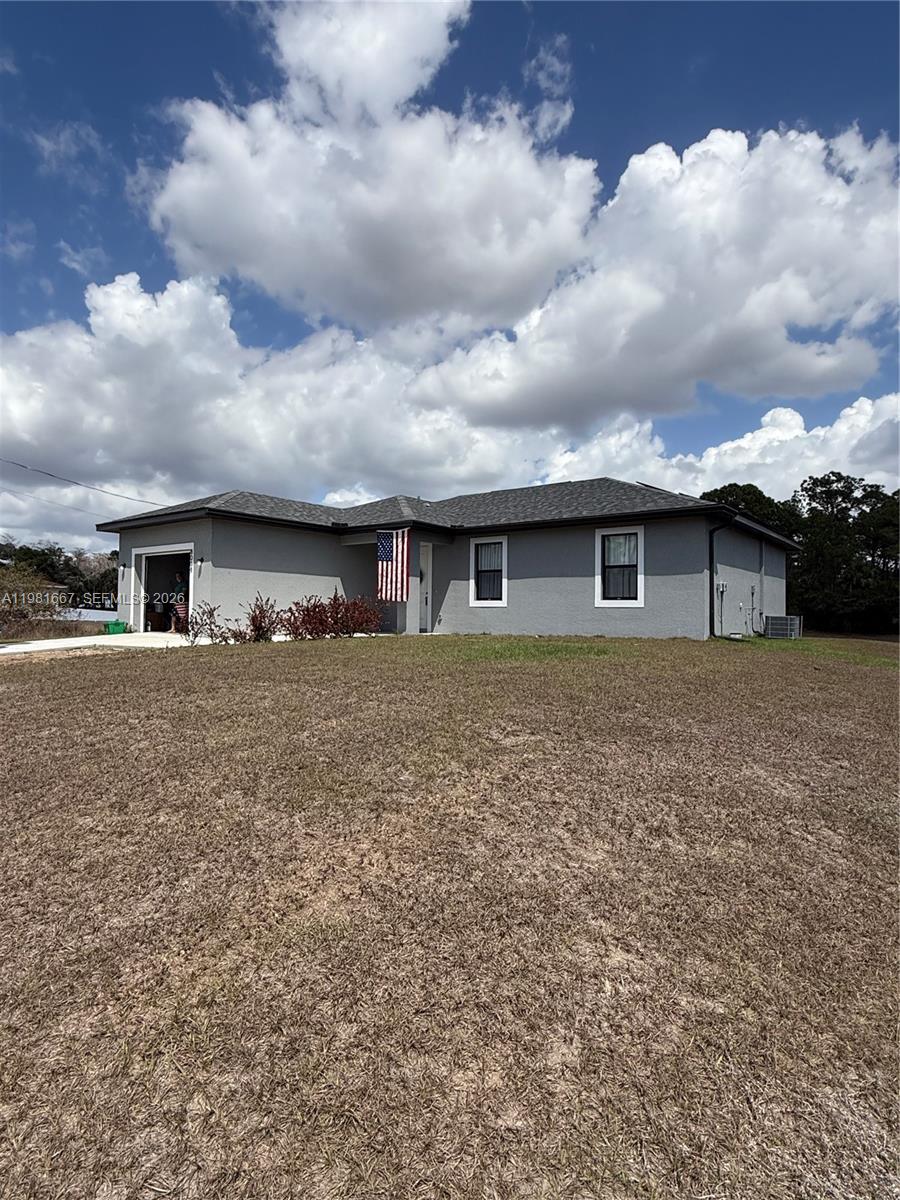 A single-story gray house with a garage and an American flag stands on a lawn — 8004 Spice CT, La Belle FL 33935, LA BELLE, FL