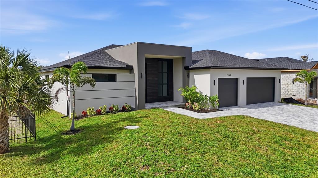 A modern single-story house with a gray exterior, dark garage doors, and a paved driveway — 9660 PRESIDENT CIRCLE, PORT CHARLOTTE, FL