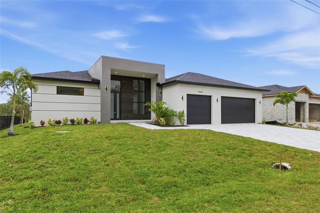 A modern single-story house with a gray facade, dark garage doors, and a landscaped lawn — 9660 PRESIDENT CIRCLE, PORT CHARLOTTE, FL