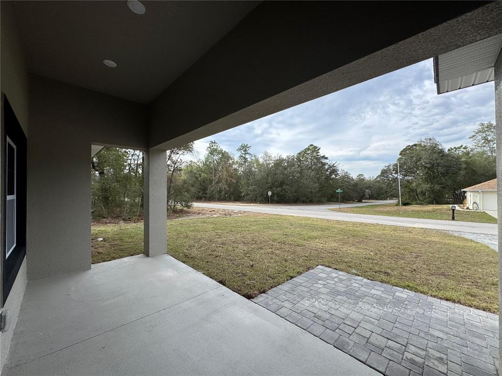 A covered concrete porch overlooks a grassy yard, a paved road, and a wooded area — 8593 N MULLER WAY, CITRUS SPRINGS, FL