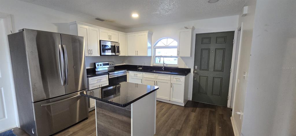 A kitchen features white cabinets, black countertops, stainless steel appliances, and a small island — 671 ROYALTY COURT UNIT A, KISSIMMEE, FL