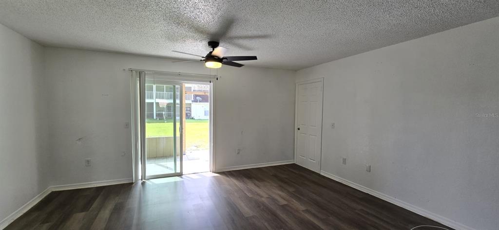 An empty room features wood-look flooring, a ceiling fan, and sliding glass doors to outside — 671 ROYALTY COURT UNIT A, KISSIMMEE, FL