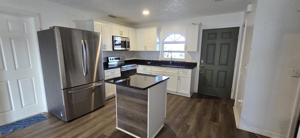 A kitchen features white cabinets, black countertops, a stainless steel refrigerator, and a center island — 671 ROYALTY COURT UNIT A, KISSIMMEE, FL