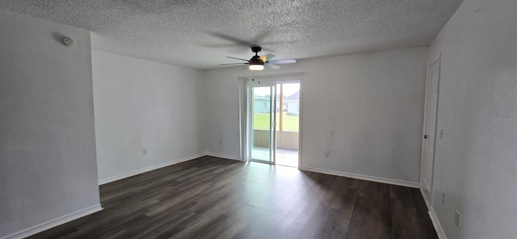 A living room with wood-look flooring, a ceiling fan, and a sliding glass door — 671 ROYALTY COURT UNIT A, KISSIMMEE, FL
