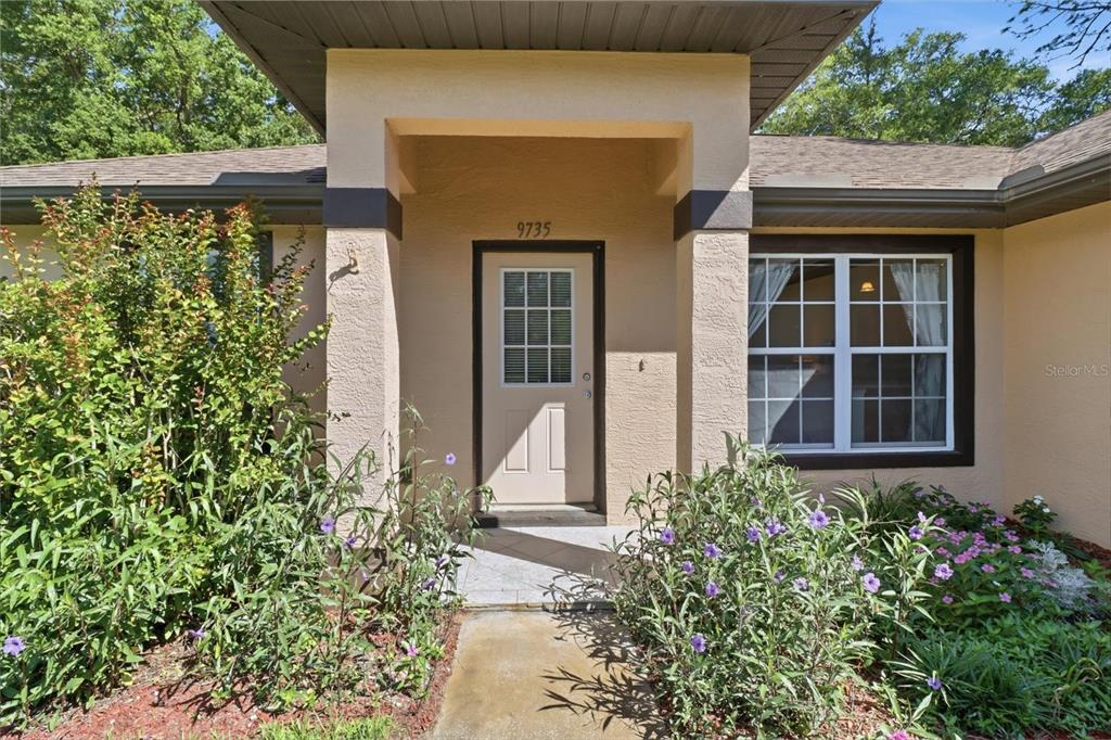 The exterior of a house features a tan stucco facade, a covered entryway, and landscaping — 9735 W DUNNELLON ROAD, CRYSTAL RIVER, FL