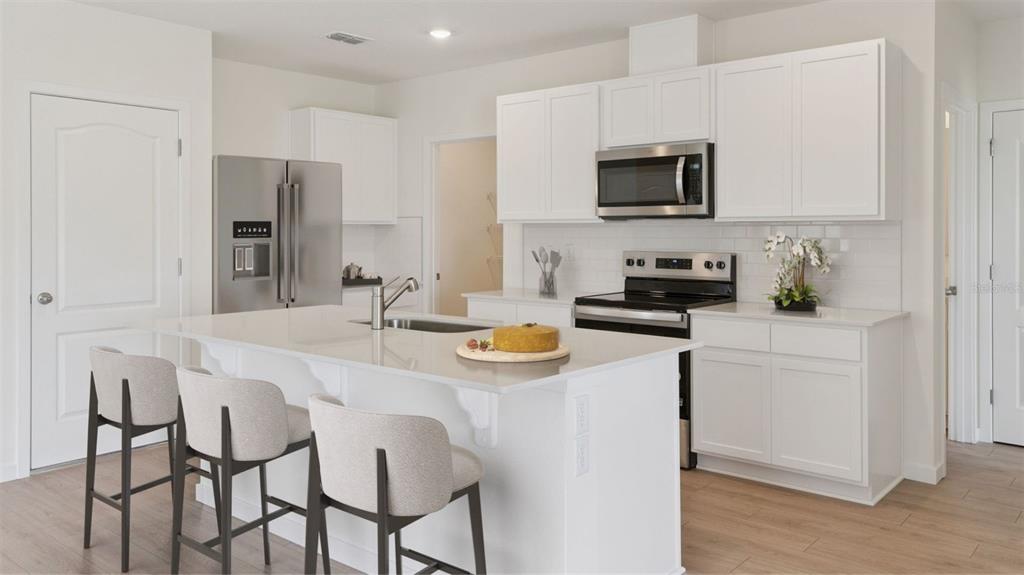 A modern kitchen features white cabinets, stainless steel appliances, a quartz island, and bar seating — 1376 GRAND FLORA LANE, SANFORD, FL