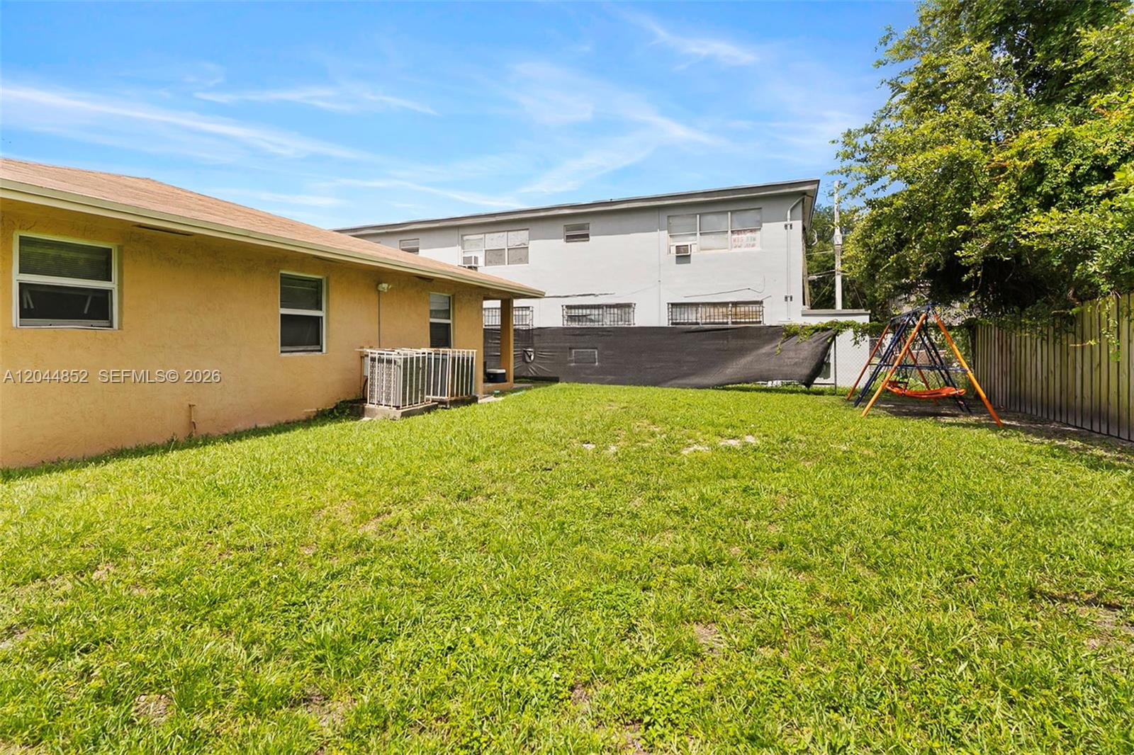 A grassy backyard features a tan house, a neighboring building, and a metal swing set — 812 NW 70th St, Miami FL 33150, MIAMI, FL