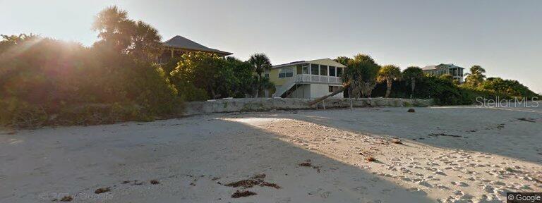 A sandy beach leads up to a low stone seawall and several elevated coastal houses — 4621 ORO PESOS LANE, CAPTIVA, FL