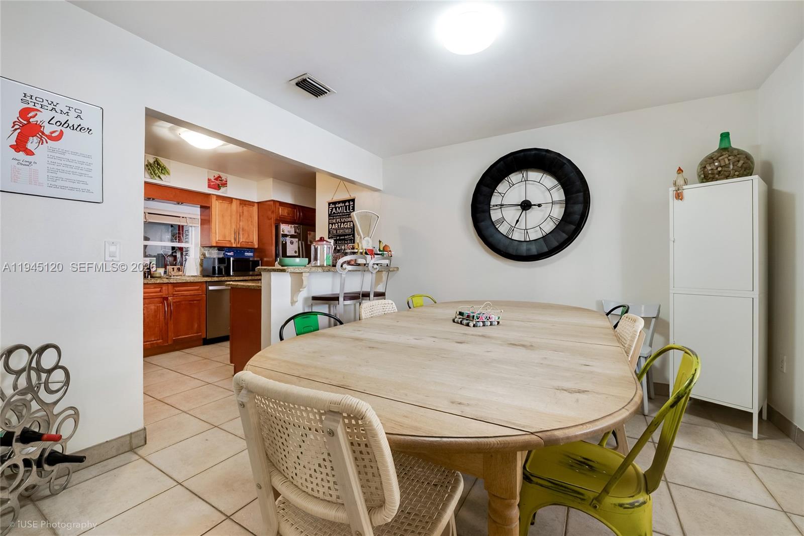 A dining area features a wooden table, mixed chairs, a large wall clock, and kitchen access — 5700 SW 45th Ter, Miami FL 33155, MIAMI, FL