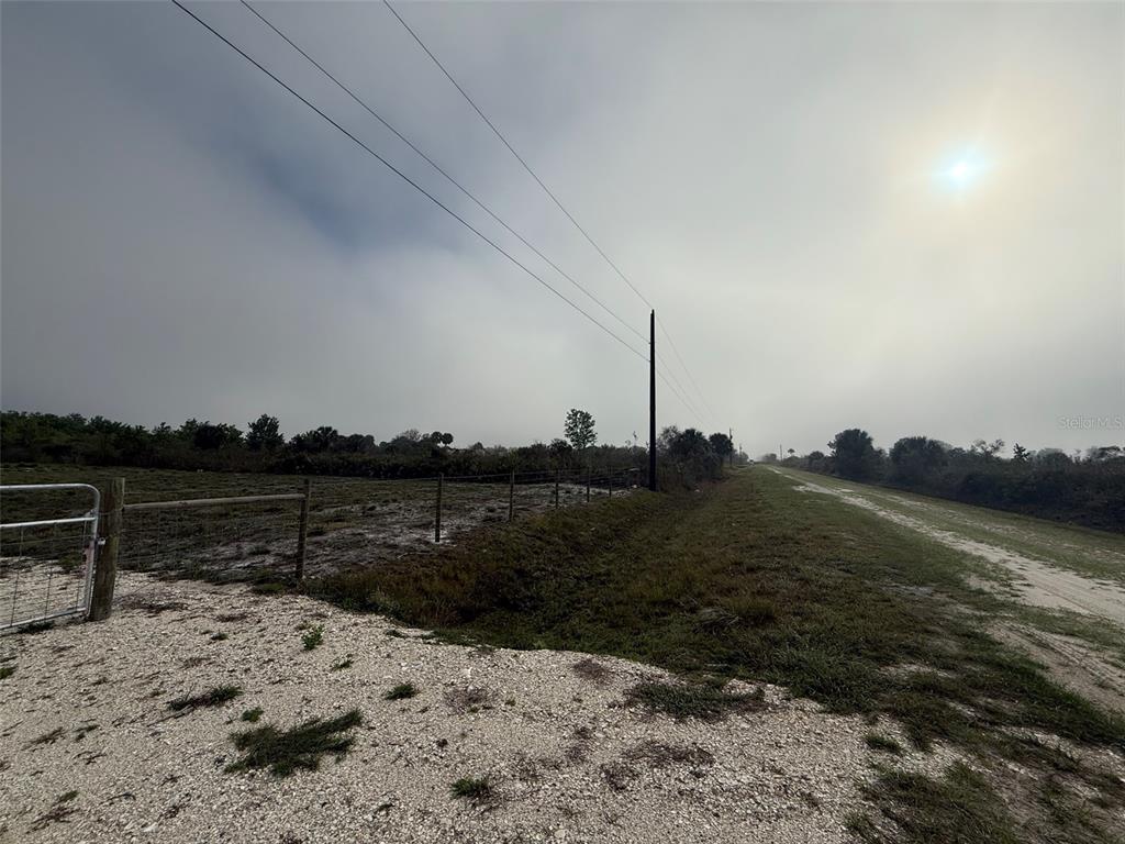 A gravel path runs alongside a fenced field under a hazy, overcast sky — 18935 NW 268TH STREET, OKEECHOBEE, FL