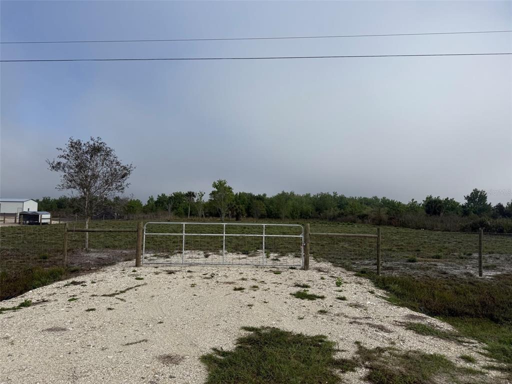 A metal gate provides access to a fenced, grassy field under a cloudy sky — 18935 NW 268TH STREET, OKEECHOBEE, FL