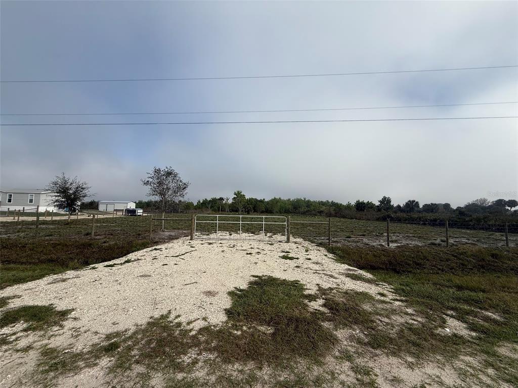 A gravel driveway leads to a metal gate opening into a large, fenced grassy field — 18935 NW 268TH STREET, OKEECHOBEE, FL