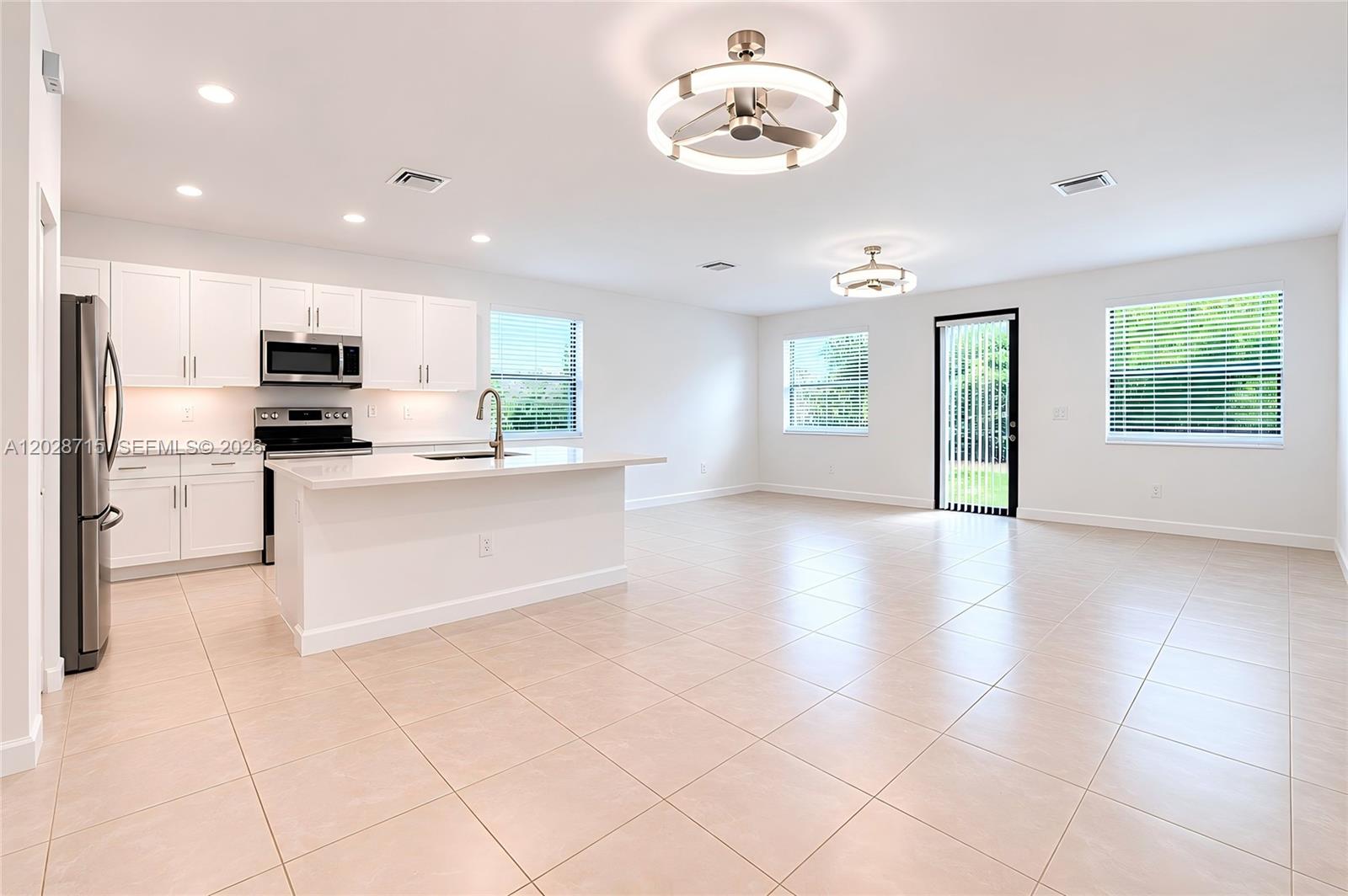 A modern kitchen with white cabinets and a central island opens into a spacious room — 3448 W 110th Ter, Hialeah FL 33018, HIALEAH, FL