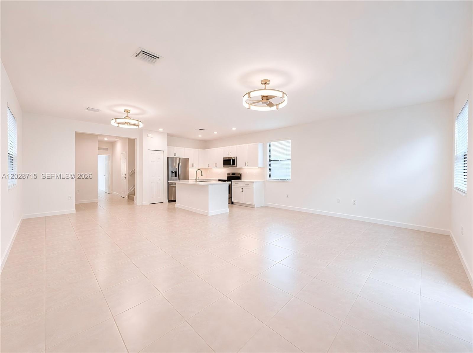 An open-concept kitchen and living area features white cabinetry, stainless steel appliances, and tile flooring — 3448 W 110th Ter, Hialeah FL 33018, HIALEAH, FL