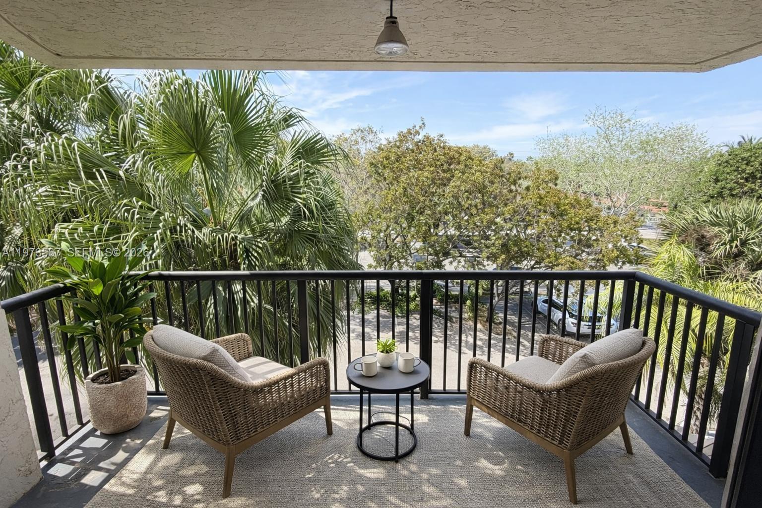 A balcony features two wicker chairs, a small round table, and a view of trees — 6601 SW 116th Ct # 402, Miami FL 33173, MIAMI, FL