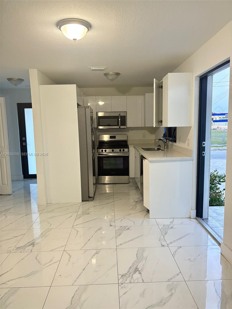 A kitchen features white cabinetry, stainless steel appliances, and white marble-patterned tile flooring — 6280 NW 22nd Ct # 2, Miami FL 33147, MIAMI, FL