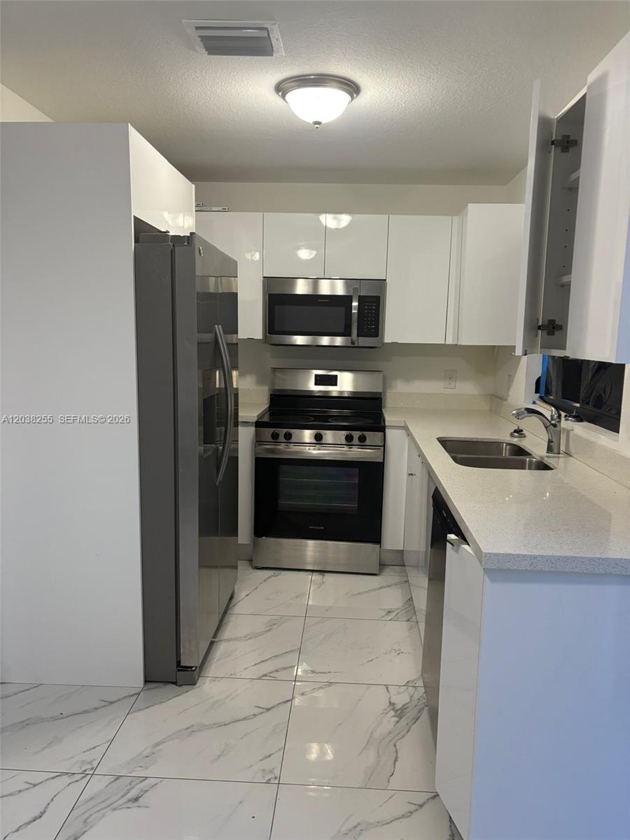 A modern kitchen features white cabinets, stainless steel appliances, and white marble-patterned tile flooring — 6280 NW 22nd Ct # 2, Miami FL 33147, MIAMI, FL