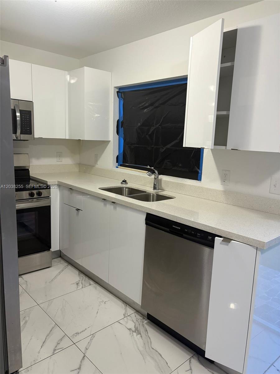 A modern kitchen features white cabinets, stainless steel appliances, and white marble-patterned tile flooring — 6280 NW 22nd Ct # 2, Miami FL 33147, MIAMI, FL
