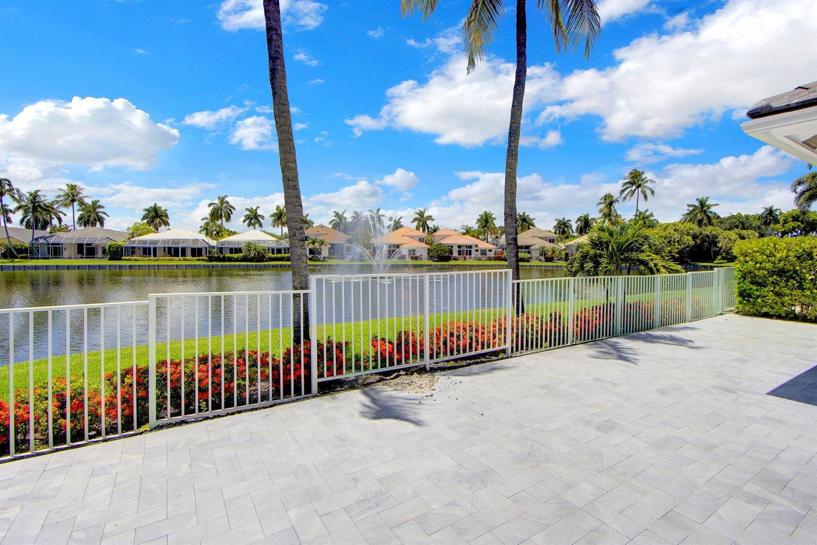 A paved patio overlooks a lake with a fountain, palm trees, and a white fence — 5463 NW 41st Terrace, Boca Raton FL 33496, BOCA RATON, FL