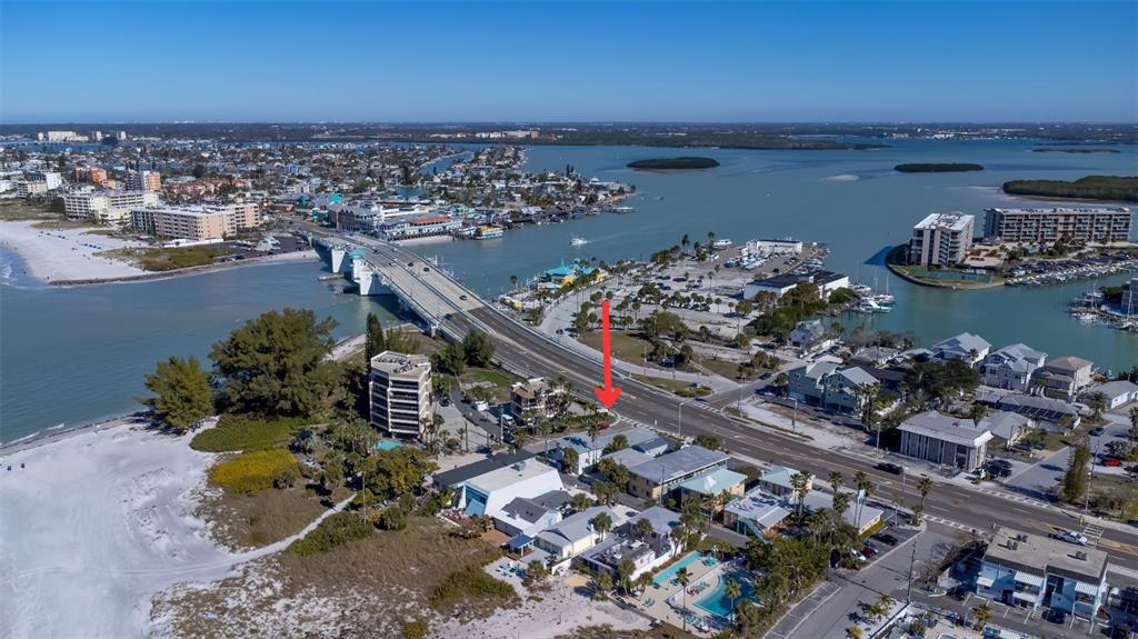 An aerial view shows a coastal area with a bridge, beach, and surrounding buildings — 12620 GULF BOULEVARD, TREASURE ISLAND, FL