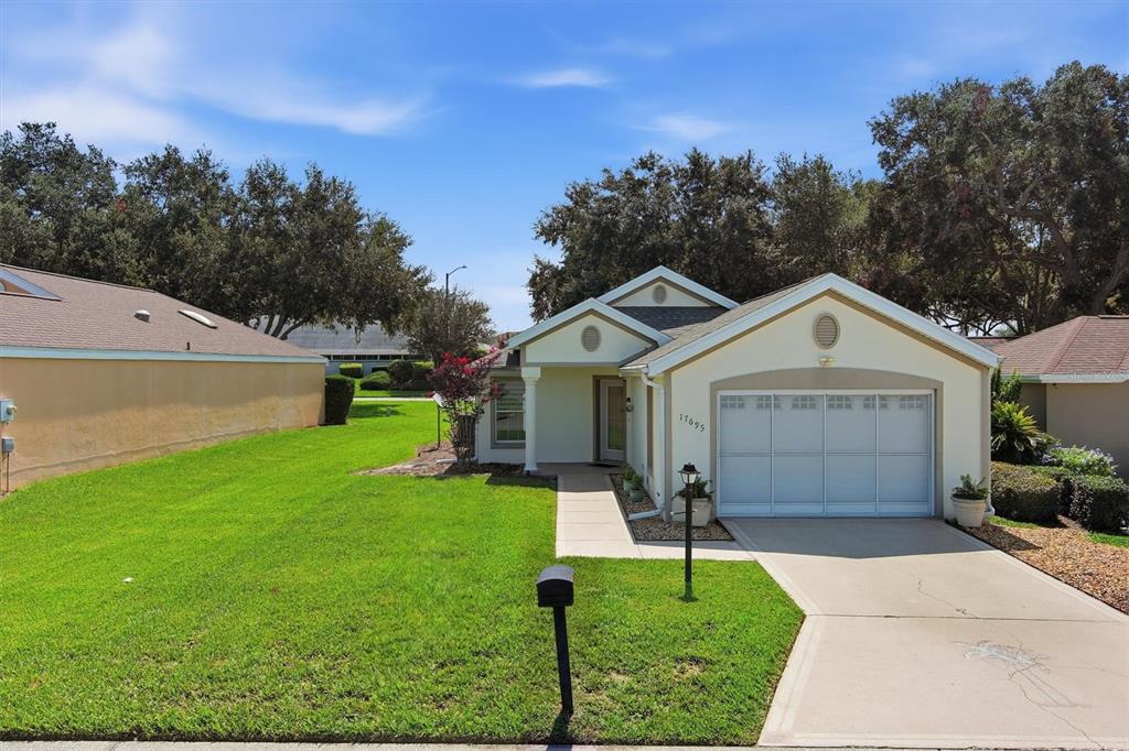 A single-story house with a beige exterior, a white garage door, and a green lawn — 17695 SE 114TH COURT, SUMMERFIELD, FL