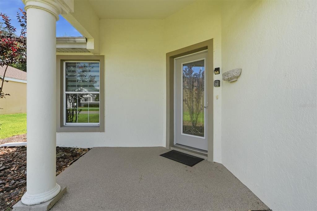 A covered front porch features a white column, a window, and a glass-paneled entry door — 17695 SE 114TH COURT, SUMMERFIELD, FL
