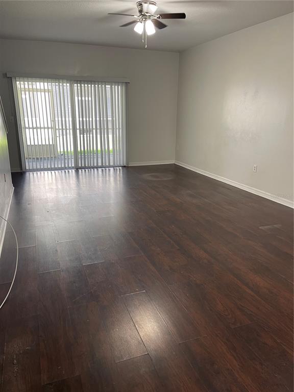 An empty living room features dark wood-look flooring, a ceiling fan, and sliding glass doors — 3548 HIGH HAMPTON CIRCLE, TAMPA, FL