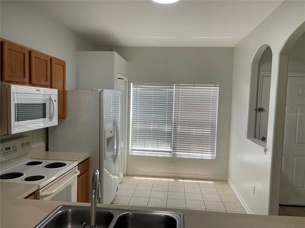 A kitchen features light-colored tile flooring, white appliances, wooden cabinets, and a window with blinds — 3548 HIGH HAMPTON CIRCLE, TAMPA, FL
