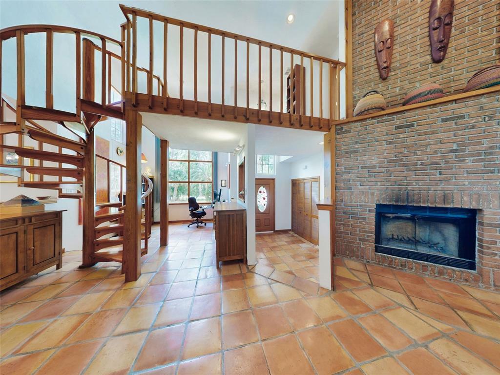 A living room with terracotta tile floors, a brick fireplace, and a wooden spiral staircase — 1205 WILLIAMS ROAD, NEW SMYRNA BEACH, FL